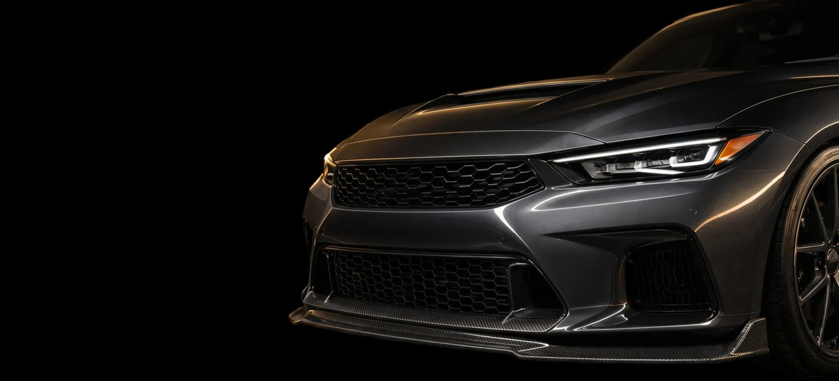 Close-up of the front bumper and grille of a dark metallic sports car on a transparent checkered background.